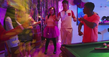 Holding sparklers, seven friends in party clothes celebrating in party room with pool table