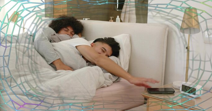 Spooning couple in bed wearing gray top and white tee, reaching for smartphone beside clock