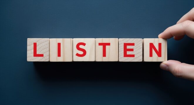 A hand spelling out the word listen using wooden blocks on a dark surface.
