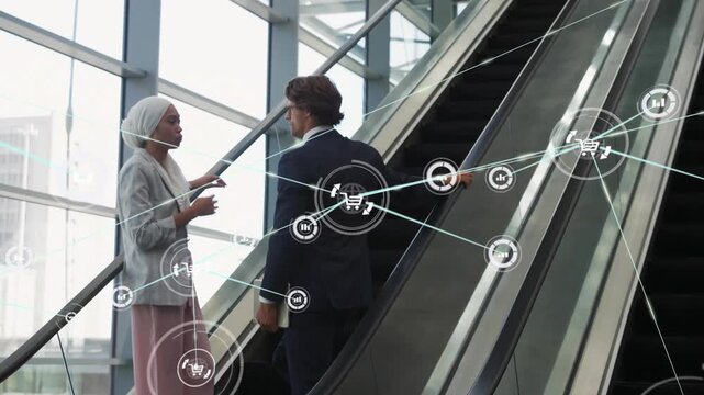 Woman in hijab gesturing to man on escalator, sparking animated biz icons showing data on tablet