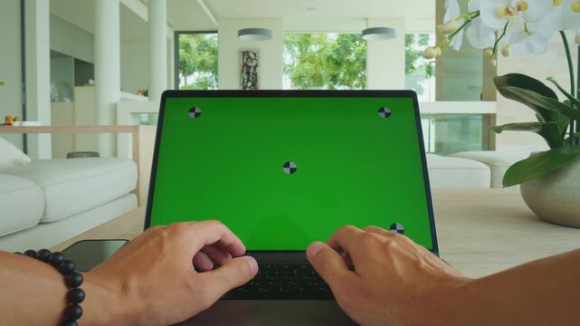 Chroma key screen on laptop used by man working at desk indoors. Chroma key screen concept represents video editing, background replacement, digital media production and mockup usage.