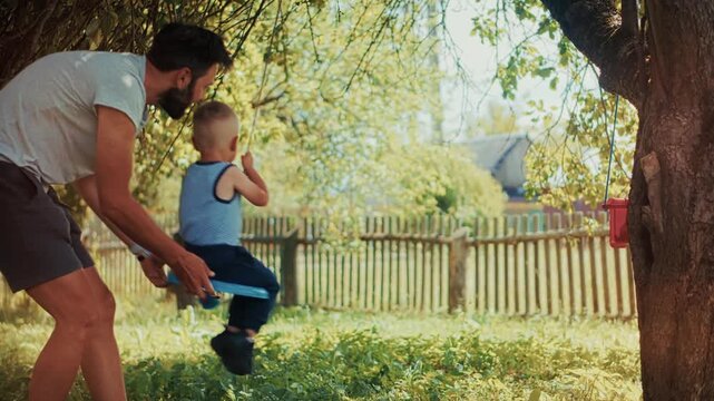 Father Pushing Toddler On Garden Swing. Active Parenthood And Family Bonds 