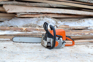 Naklejka premium Orange professional chainsaw lying on snow next to wooden planks
