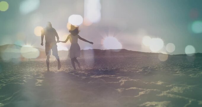 Couple holding hands walking across sand to horizon sun causing bokeh flare overlay for marketing