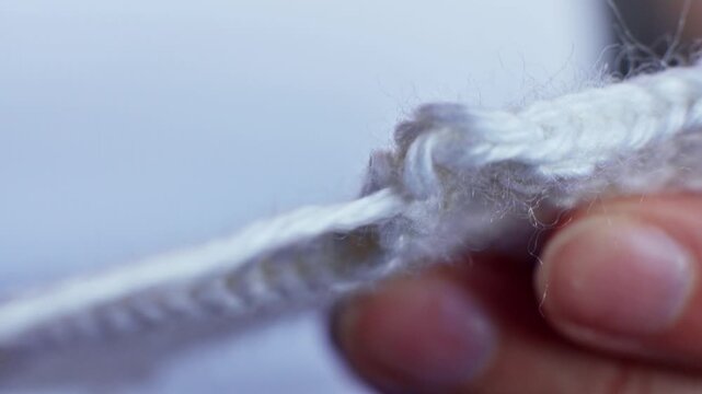Close-up of hands manipulating white yarn, showing the progression of knotting technique with visible fibers and texture in a well-lit indoor setting