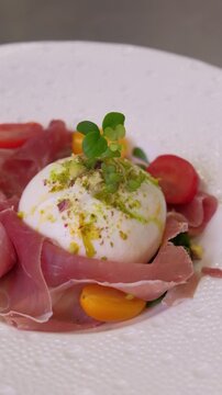 Close up of fresh burrata cheese salad preparation process. Unrecognizable chef of italian restaurant preparing for serving starter from seasonal menu. High quality FullHD footage