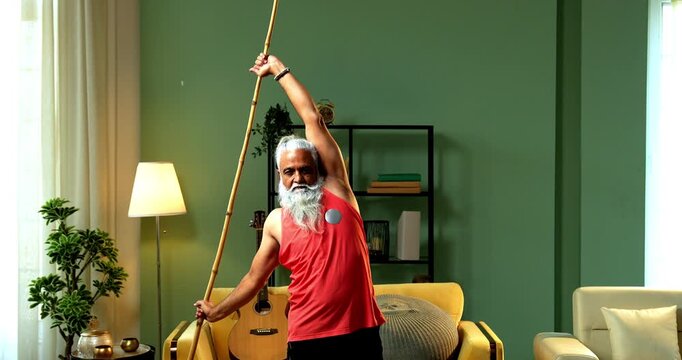 Indian mid age stylish bearded man doing exercise using stick, rod or staff at home, fitness conscious mature male performing strength and mobility workout showing agility and determination