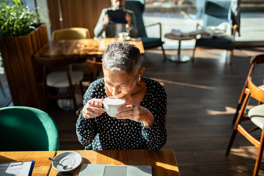 Senior woman drinking coffee in sunny cafe