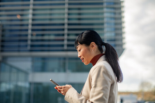 Businesswoman using smartphone outside modern office building