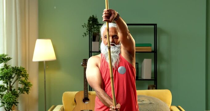 Indian mid age stylish bearded man doing exercise using stick, rod or staff at home, fitness conscious mature male performing strength and mobility workout showing agility and determination