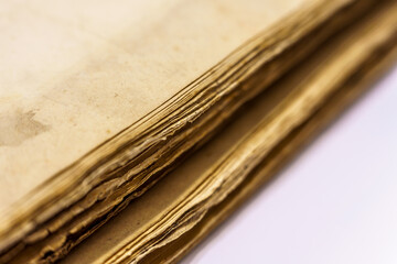 Makro zbliżenie na róg starej, pożółkłej księgi lub stosu archiwalnych dokumentów. Widoczne tekstury zniszczonego papieru i warstwy historii. Antyczny, vintage styl na białym tle.