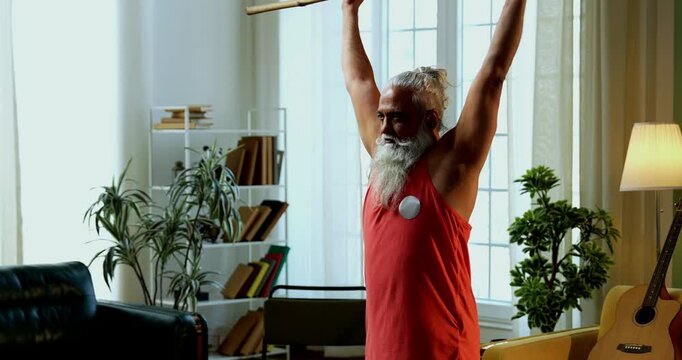 Indian mid age stylish bearded man doing exercise using stick, rod or staff at home, fitness conscious mature male performing strength and mobility workout showing agility and determination