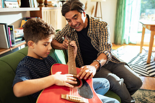 Man teaching boy acoustic guitar at home