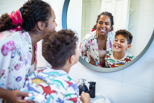 Smiling mother and son brushing teeth in home bathroom mirror
