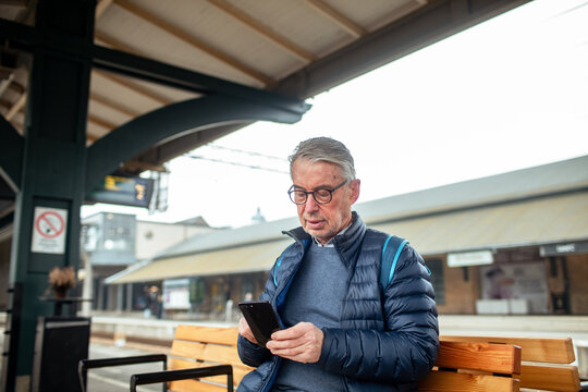 Senior man using smartphone while waiting at train station platform