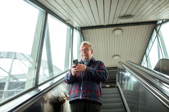 Senior man using smartphone on escalator at transit station