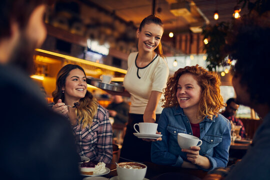 Friends enjoying coffee while waitress serves in cozy cafe