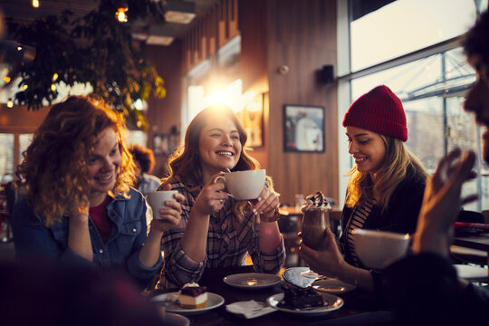 Happy friends enjoying coffee and dessert at a sunlit cafe