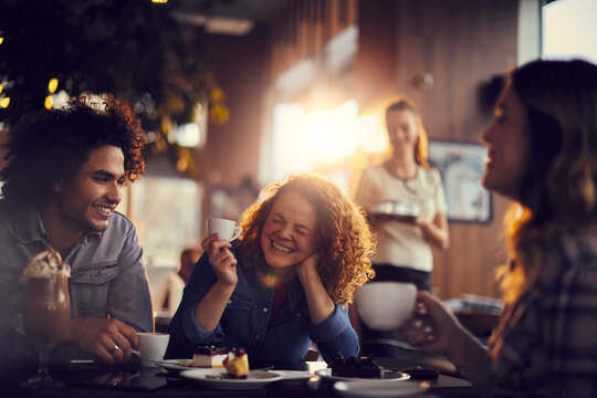 Friends laughing over coffee and dessert in cozy cafe