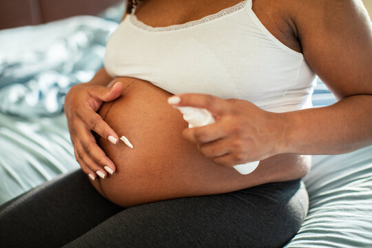 Pregnant woman applying belly lotion at home