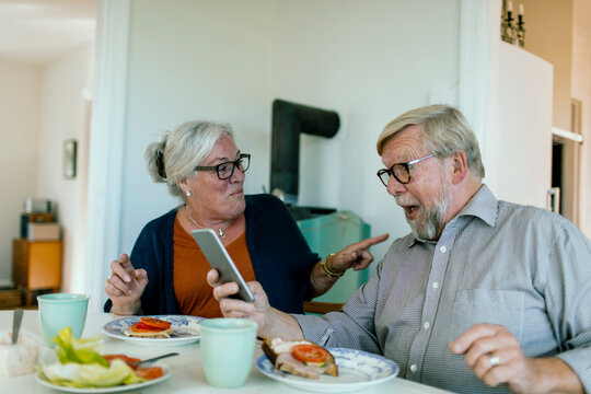 Surprised senior couple reacting to smartphone at home kitchen table