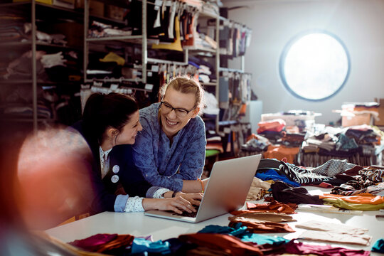 Two fashion designers collaborating with laptop in fabric studio