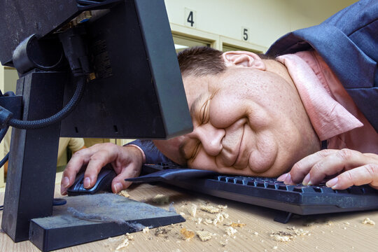 Lazy office worker dozing with his head resting on the keyboard in an office with dispensing windows in the background