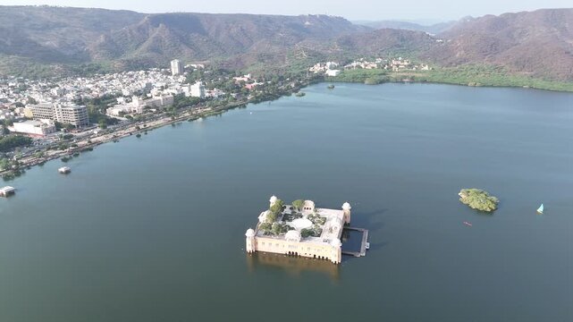 Aerial drone orbit around Jal Mahal palace located in Man Sagar Lake in Jaipur, Rajasthan, India. Scenic landscape with historic architecture, calm water and mountains in the background.