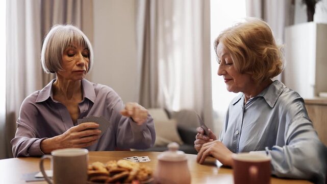 Senior women friends playing cards at home, smiling female winning a game