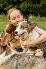 Obraz premium Professional dog walker young woman with pack of dogs is sitting on green grass and enjoying walk with animals. training and upbringing and care of pets. dogs from the shelter.