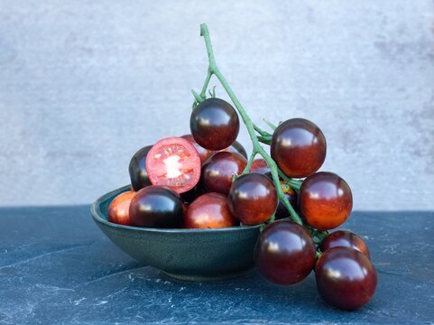 Black tomatoes of Indigo Rose in a bowl on the stone table. This natural form is rich in anthocyanin in black peel and good for our health.