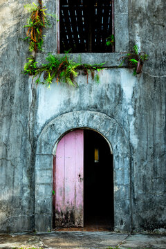 The facade of an old, abandoned concrete building with arched doors and windows.
