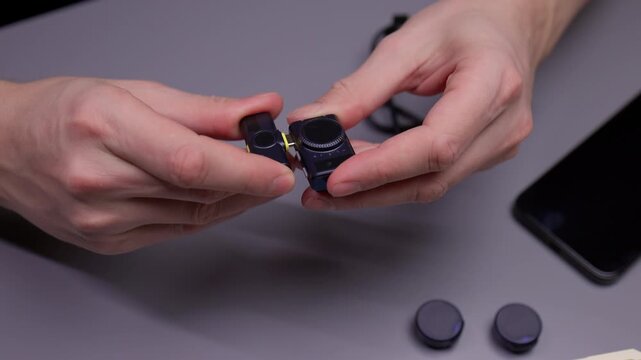 Close-up of unrecognizable man connecting small compact wireless microphone system, assembling audio gear for recording sound and ensuring proper function for broadcasts or online content creation.