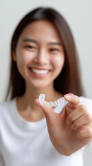 Asian young female holding clear dental aligner with smile