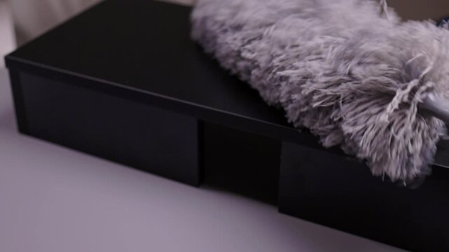 Gray microfiber duster collecting particles from newly assembled black wooden furniture surface, emphasizing importance of housekeeping and maintenance for tidy home environment.