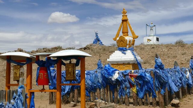 Santmargats, MONGOLIA - July 18, 2017. The Buddhist stupa and prayer wheels against the background of oboo (ovoo, ritual heap of stones) and the sculpture of a woman under a picturesque cloudy sky.