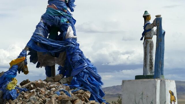 Santmargats, MONGOLIA - July 18, 2017. Ritual pile of stones (ovoo, oboo) and sculpture women c with a scarf in their hands against the backdrop of a picturesque cloudy sky and mountains.
