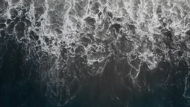 Atlantic waves crashing onto rocky pebble coast, dynamic ocean motion from drone above water