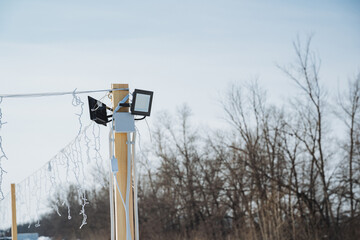 Wooden Pole Lighting. Utility Pole With Multiple Lighting Elements And Winter Scenery. Structures Supporting Illumination And Seasonal Decorations Against Overcast Winter Background