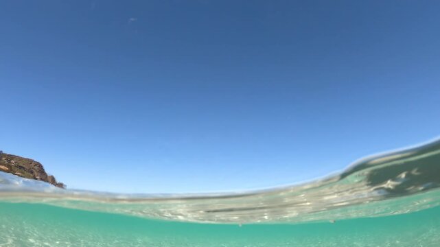 Split level underwater view of turquoise water at La Pelosa beach in Stintino, showing crystal clear Mediterranean sea above and below the surface in bright natural light.