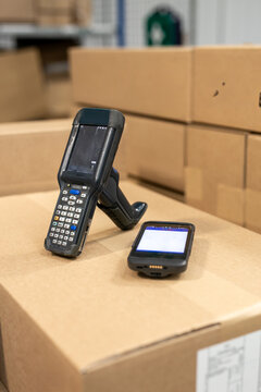 Two different types of warehouse RFT terminals and barcode scanners placed on a cardboard box in the warehouse