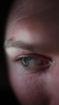 Vertical screen close up of a human eye illuminated by soft phone light while staying up late staring at the device with visible fatigue subtle reflections and detailed low light skin texture