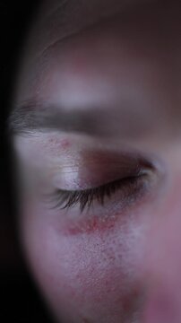 Vertical screen close up of a human eye gently closed after falling asleep while watching short videos soft phone light fading across the eyelid and detailed low light texture on resting skin