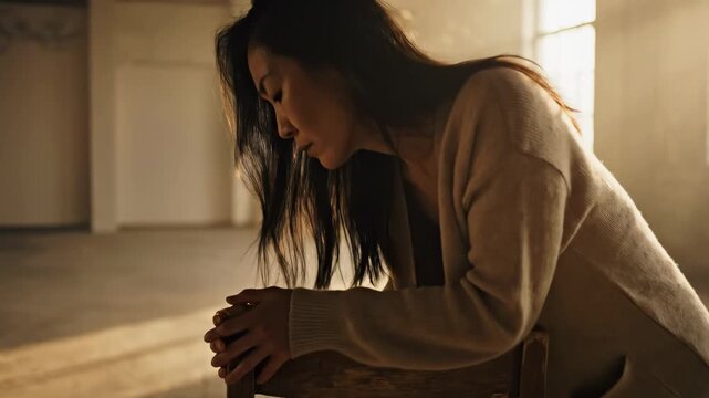 Woman in distress leaning on chair in empty room.