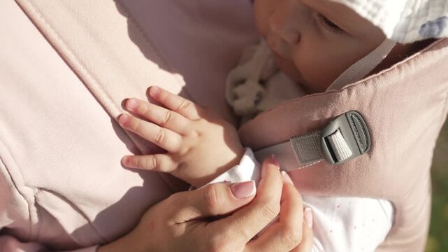 Mom and Baby Girl Holding Hands in Ergonomic Carrier Outdoors, Close Up Details