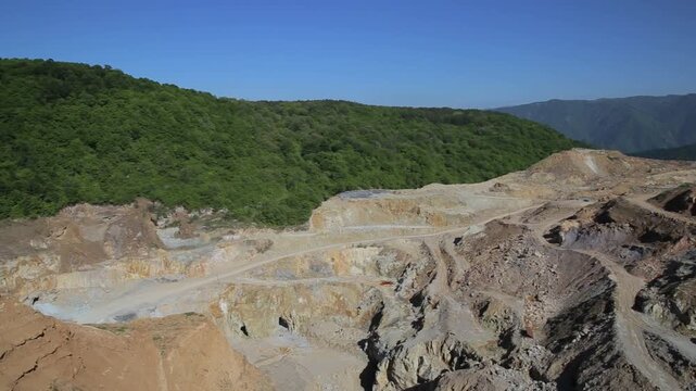 Aerial view looking into a deep open pit mine. A slow camera tilt reveals the rugged, excavated landscape with winding dirt tracks, exposed rock layers, and steep drop-offs.

