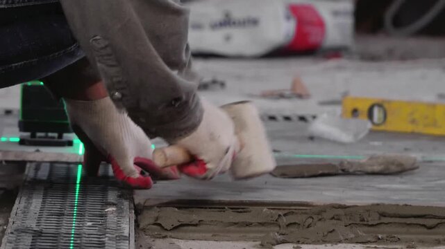 Professional builder worker installing floor a large ceramic tile using a laser level. Man experienced repairman laying placing tile indoors house or apartment. Worker Laying Ceramic Tiles.