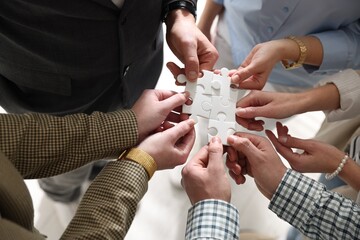 Team building. Group of businesspeople holding puzzle pieces together on blurred light background, above view