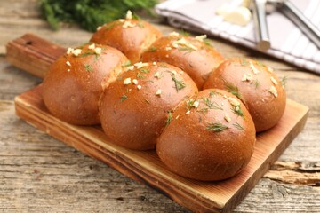 Tasty baked buns with garlic and dill on wooden table, closeup