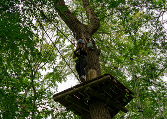 Fototapeta premium Young woman stepping forward on treetop platform in adventure park